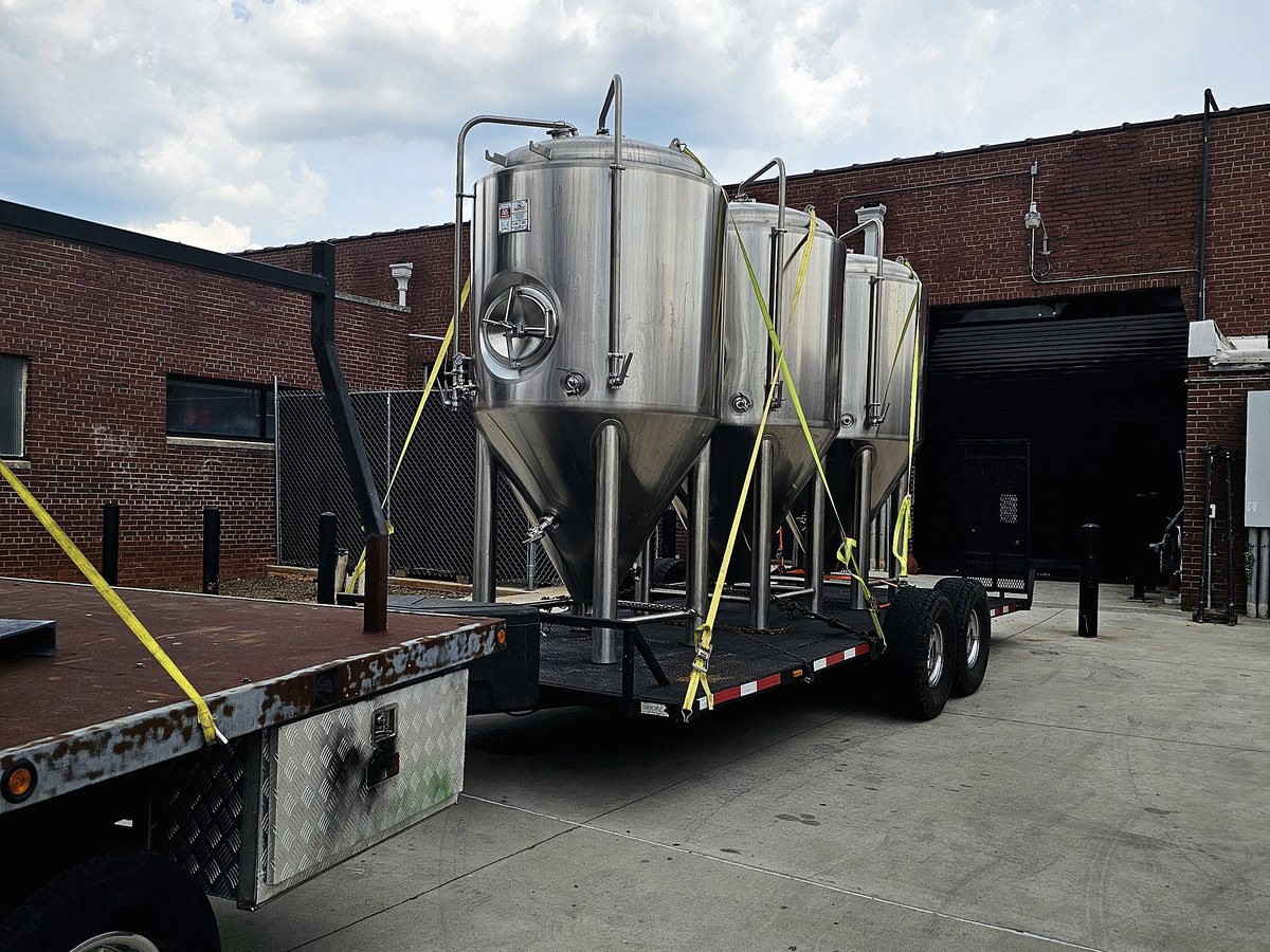 Three conical fermenters strapped upright on a flatbed trailer